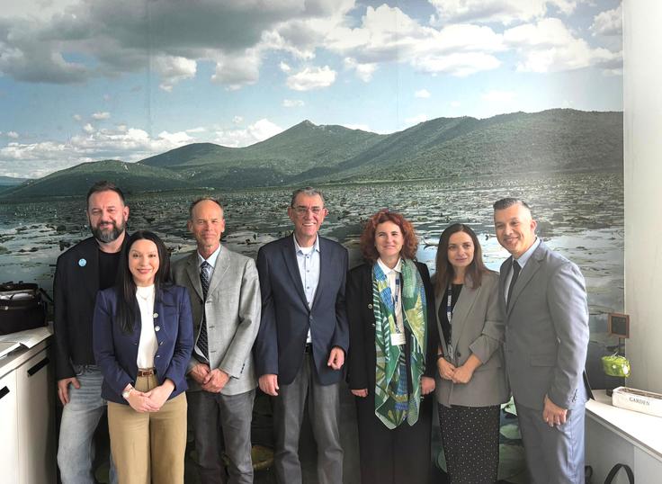 Seven people smiling in business attire, standing in front of a mountain landscape mural.