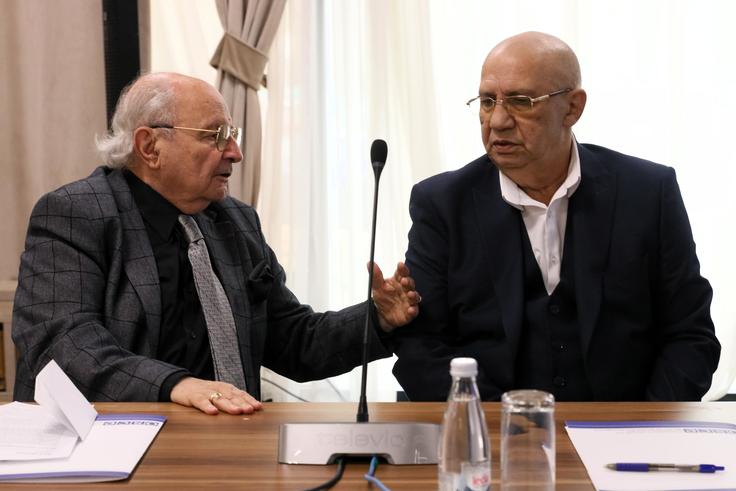 Two men in suits sitting at a conference table, engaged in conversation.