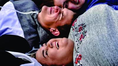 Three people lying close together, smiling and laughing, wearing sweaters with varying patterns.