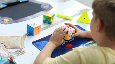 A child in a yellow shirt solves a Rubik's Cube on a table with other puzzles.