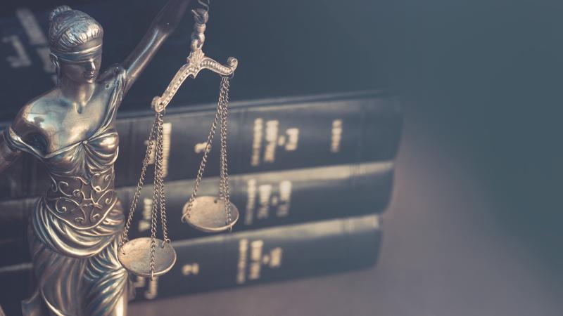 Figura pravde s vagom ispred tri knjige zakona na tamnoj pozadini.