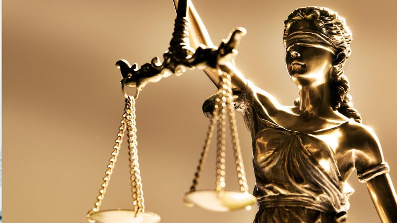 Blindfolded Lady Justice statue holding balanced scales, warm golden hue.