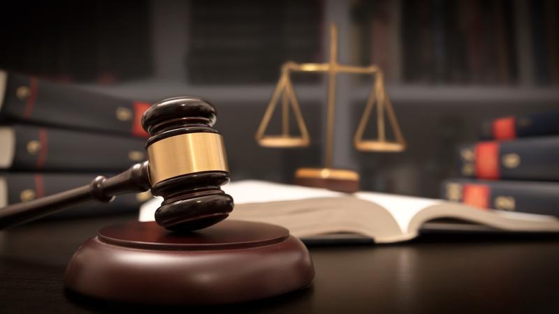Gavel and scales of justice on a desk with open law book and stacked books in the background.