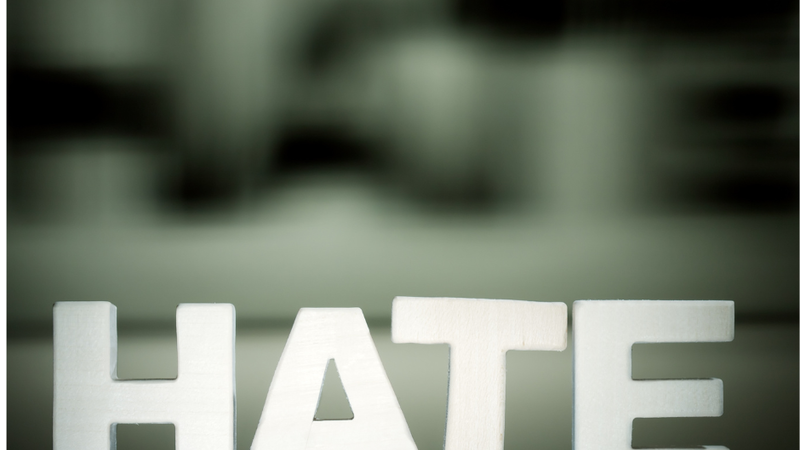 Block letters spelling "HATE" on a reflective surface, blurred background.