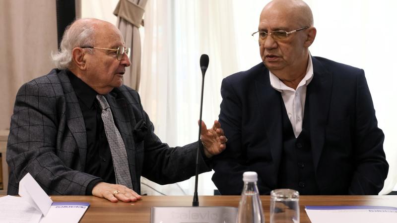 Two men in suits sitting at a conference table, engaged in conversation.
