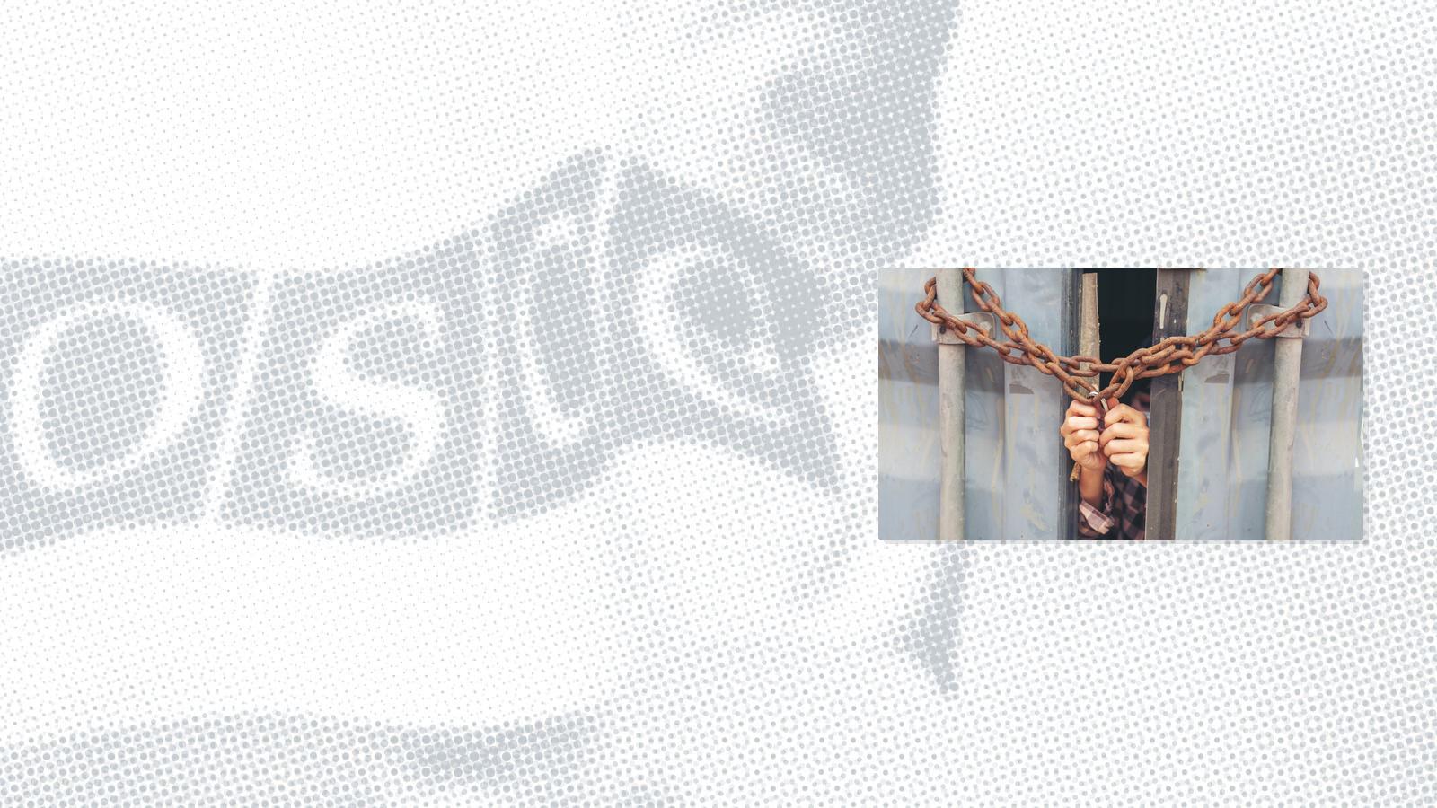 Hands gripping iron bars through a chained and locked gate.