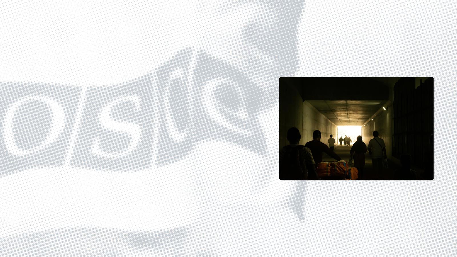 Silhouettes of people walking through a dimly lit tunnel toward bright light, some carrying bags.