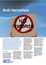 Hands hold a sign with "No Terrorism" in a red circle and slash, against a blue sky.